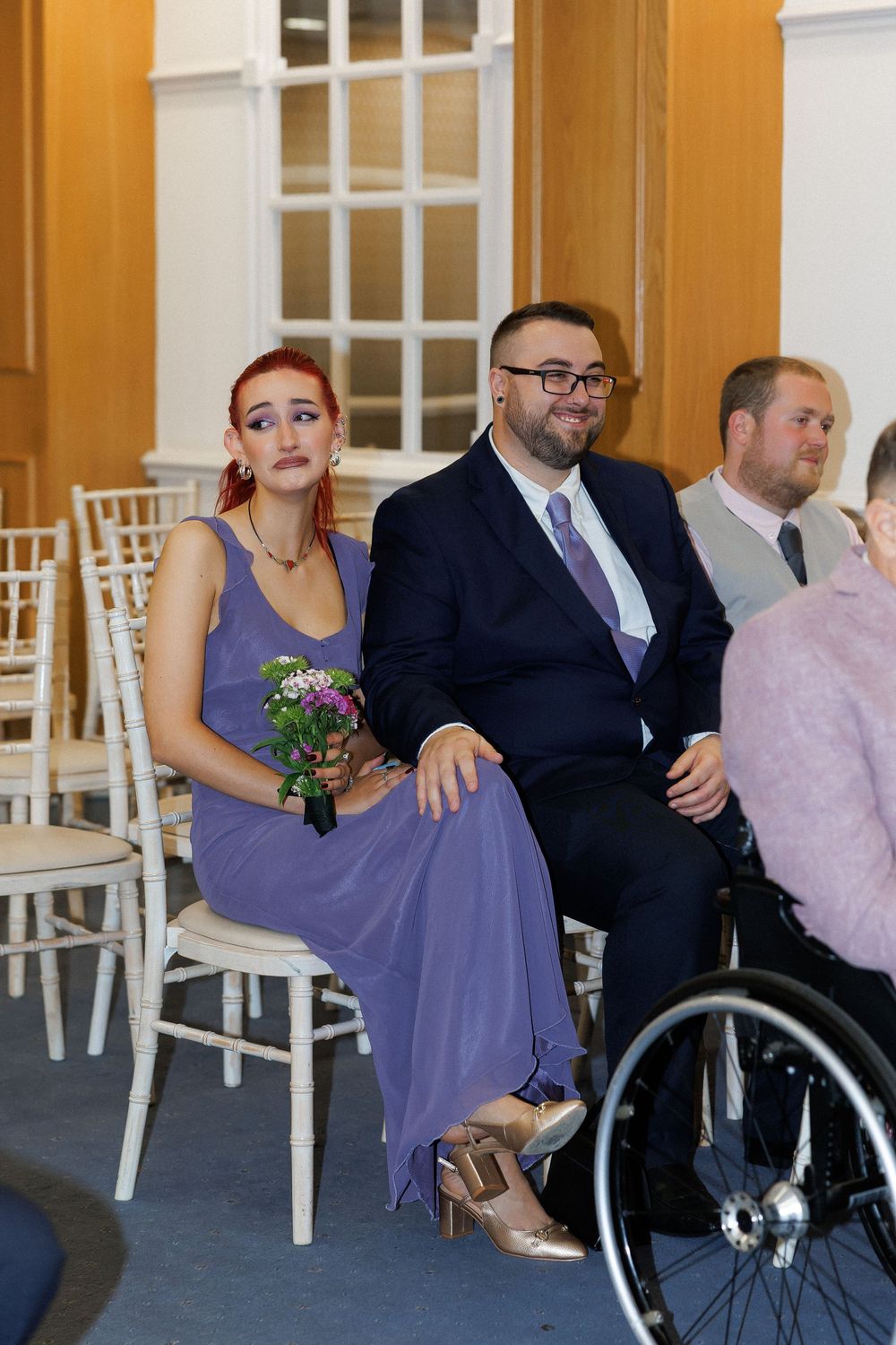 Wedding guests in formal attire seated at a ceremony, including a woman in a purple dress.