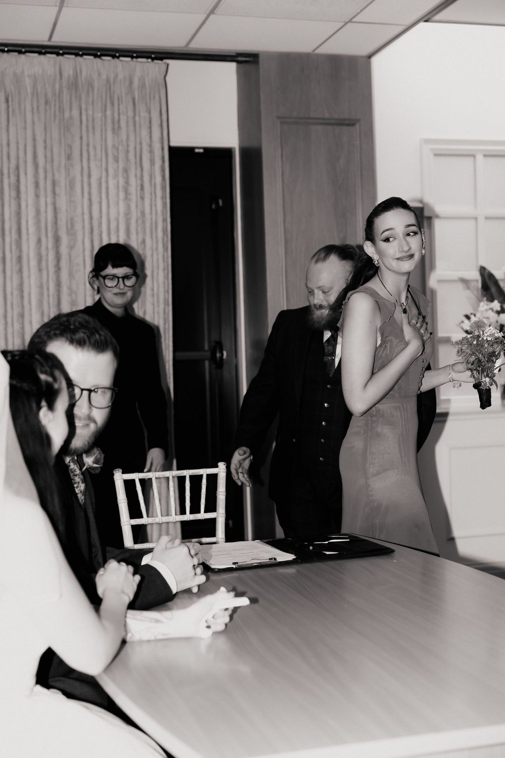 Black and white photo of wedding guests signing marriage documents at a table during an intimate ceremony.