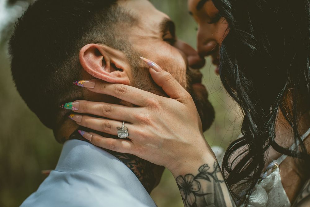 Close-up of a couple sharing a romantic moment, woman's hand with green nails and diamond ring cradling man's tattooed neck.