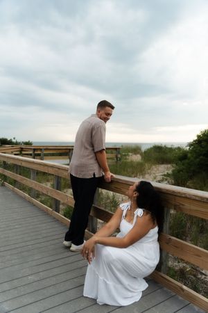Couple on a beach boardwalk, woman in white dress seated by railing, Located in Connecticut at Harkness State Park