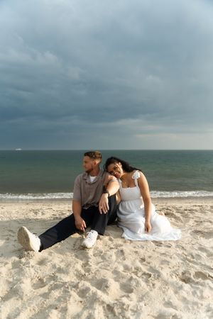 Couple sitting together on sandy beach with cloudy sky and ocean waves, Located in Connecticut at Harkness State Park