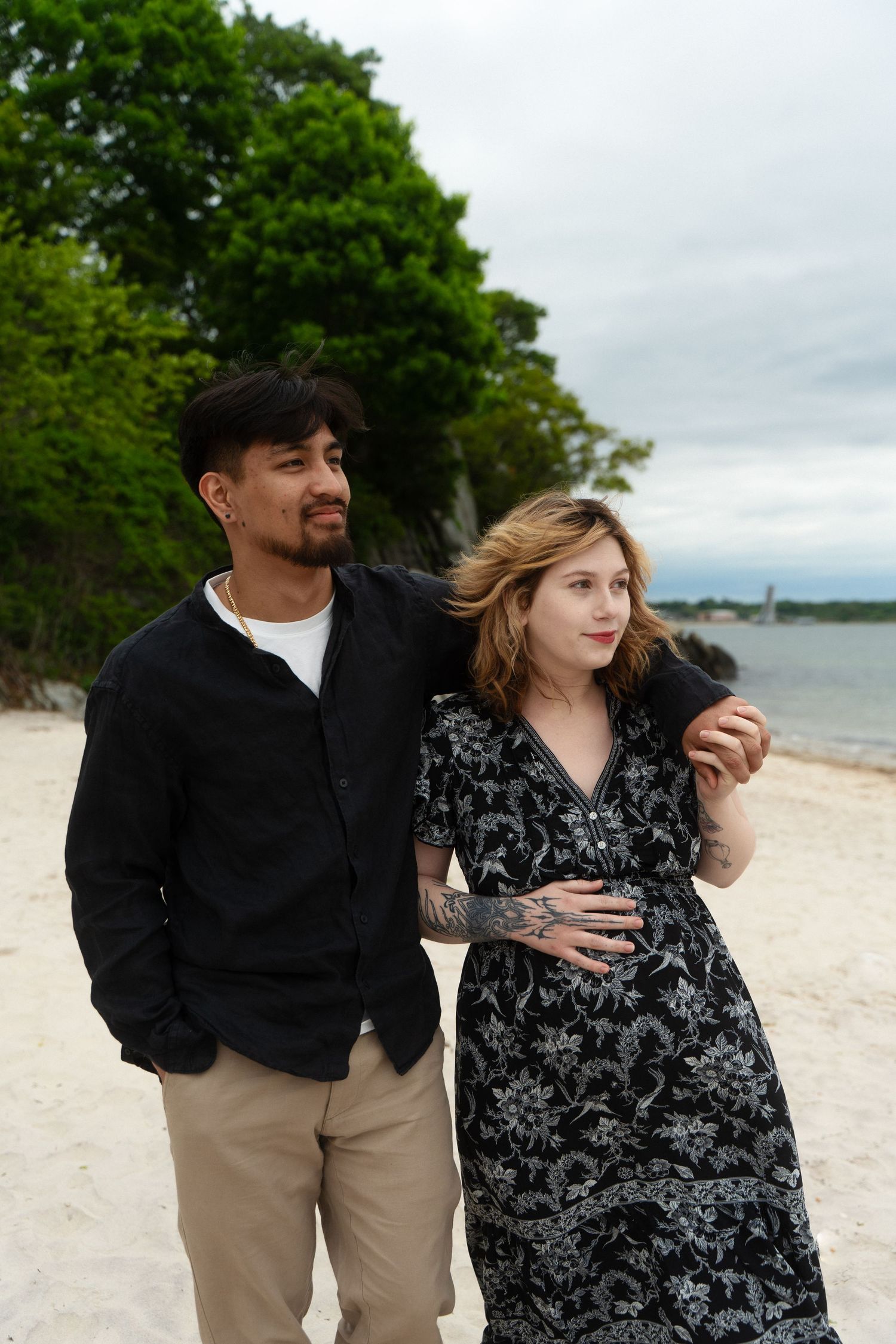 A couple stands on a sandy beach, the woman in a floral dress McCook Beach in Niantic Connecticut