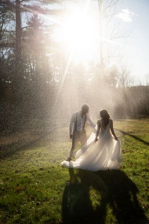 Bride and groom walk hand-in-hand through sunlit rain session in Westerly Rhode Island.