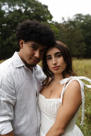 A young couple in white outfits pose together in a lush green field, Flower field located in Connecticut