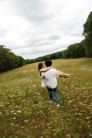 A man carries a woman in his arms while spinning in a blooming wildflower meadow Flower field located in Connecticut