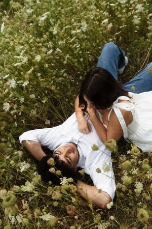 Romantic couple lying in a wildflower meadow, woman leaning over smiling man among white blooms. Flower field located in Connecticut