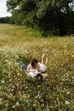 A couple playfully falls together into a field of white wildflowers with green trees in the background. Flower field located in Connecticut