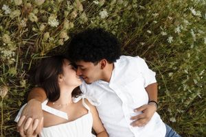 Romantic couple lying in a flower field sharing a kiss, wearing white outfits surrounded by wildflowers. Flower field located in Connecticut