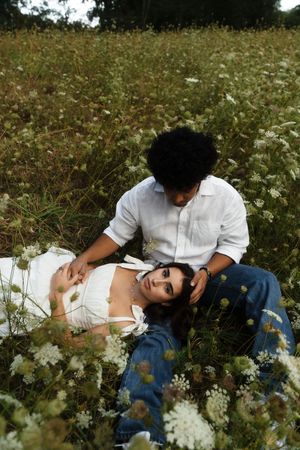 Couple in white shirts and jeans relaxing in a wildflower field, woman lying in mans lap outdoors. Flower field located in Connecticut