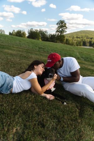 Couple lying on green grass with their black and white dog on a sunny day with blue skies. Candlelight Farms located in Connecticut