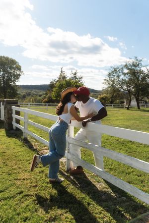 Couple sharing a romantic moment leaning against a white fence on a sunny farm. Candlelight Farms located in Connecticut