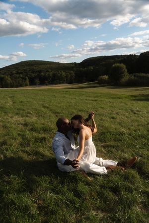 Couple sitting in lush green field, golden hour with rolling hills and clouds. Candlelight Farms located in Connecticut