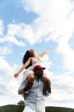 Woman with arms raised joyfully sitting on mans shoulders against a blue sky. Candlelight Farms located in Connecticut