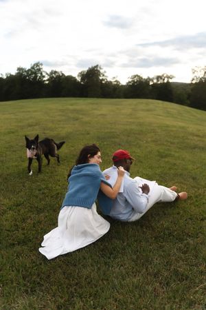 Couple sitting on green grass field with a black and white dog nearby. Candlelight Farms located in Connecticut