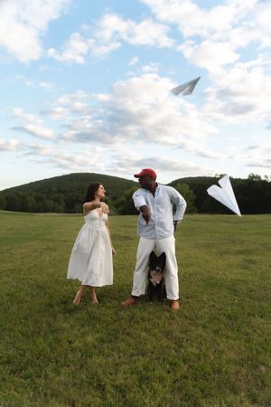 Couple standing in green field throwing paper airplanes with their dog on a cloudy day. Candlelight Farms located in Connecticut