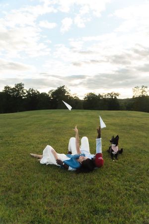 Couple lying on grass tossing paper airplanes with their dog beside them in an open field. Candlelight Farms located in Connecticut