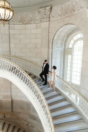 Couple in wedding attire walking up elegant curved marble staircase in grand historic building. Hartford city hall located in Connecticut