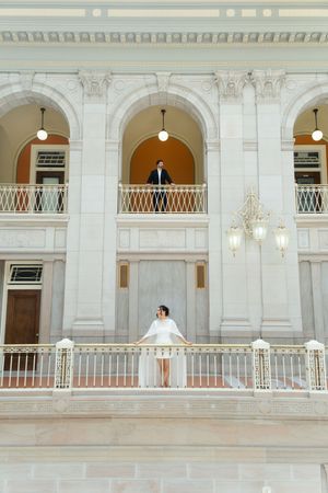 Bride in white dress on balcony with groom overlooking ornate classical architecture above. Hartford city hall located in Connecticut