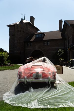 Bride's wedding veil draped over a vintage pink convertible car outside an elegant stone mansion. Ocean Cliff in Newport Rhode Island