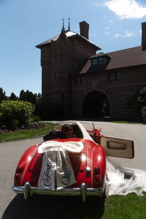 Newlyweds in a classic red convertible with Just Married sign outside a stone castle venue at Ocean Cliff in Newport Rhode Island