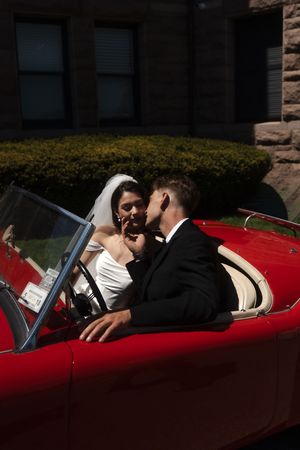Newlywed couple sharing a romantic moment in a classic red convertible, at Ocean cliff in Newport rhode island