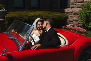 Bride and groom share a romantic kiss in a classic red convertible sports car on their wedding day. Ocean Cliff in Newport Rhode Island