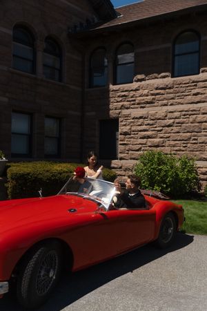 Couple in a classic red convertible sports car parked outside a stone building on a sunny day. Ocean Cliff in Newport Rhode Island