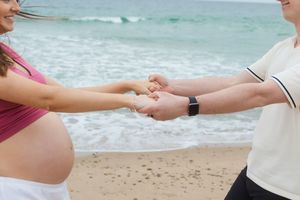 Pregnant woman in pink top holding hands with partner at Watch Hill Beach in Rhode Island.