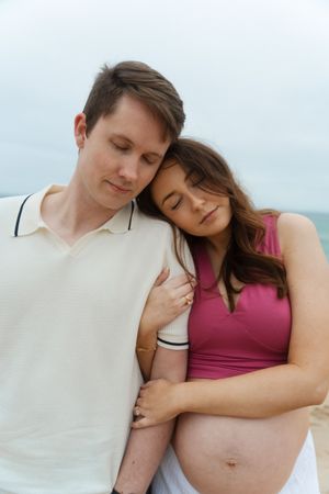 Couple sharing tender moment on beach, pregnant woman in pink top at Watch Hill Beach in Rhode Island.