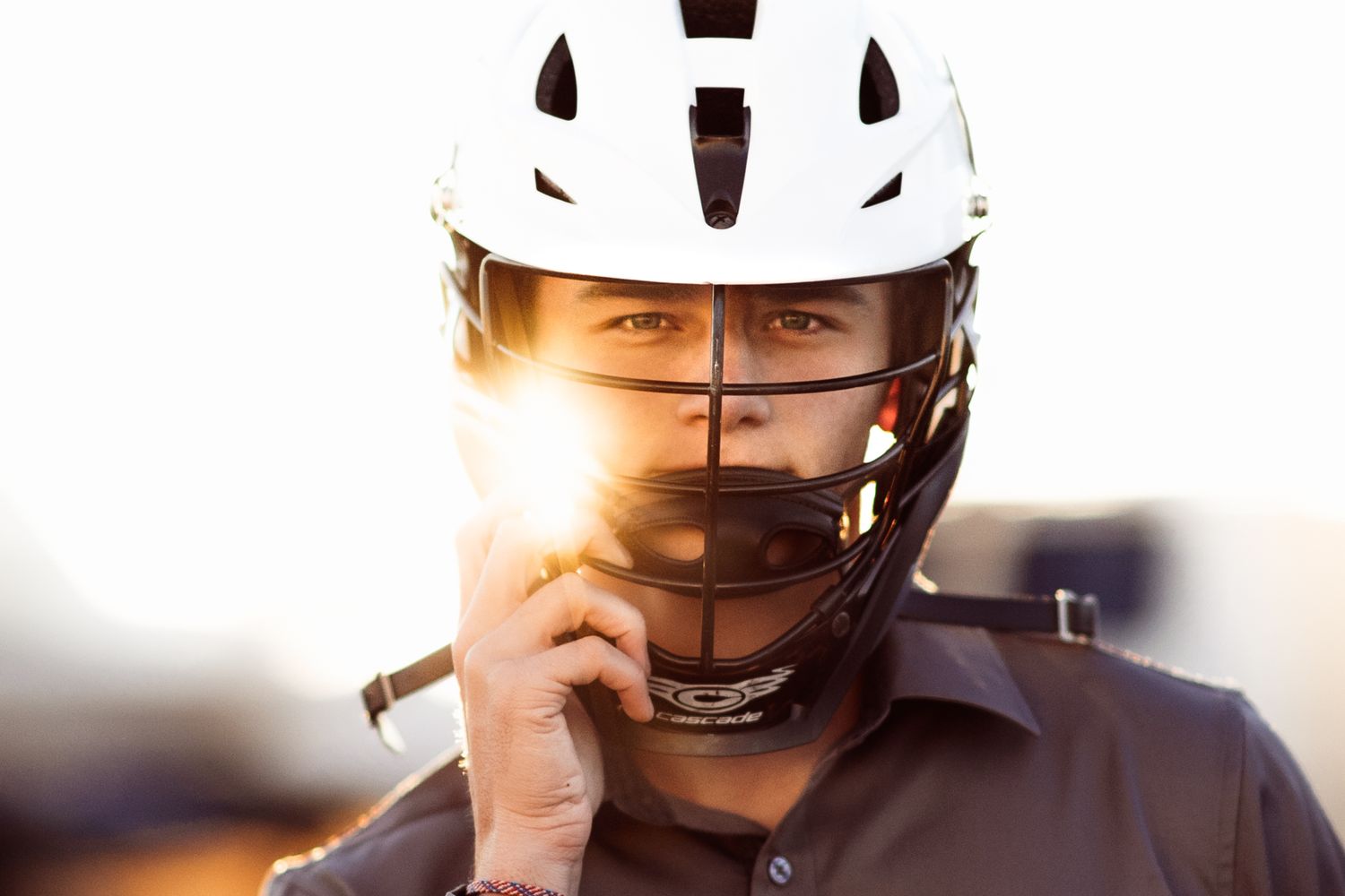 Athlete wearing a white lacrosse helmet with face guard, backlit by golden sunlight in a dramatic portrait.