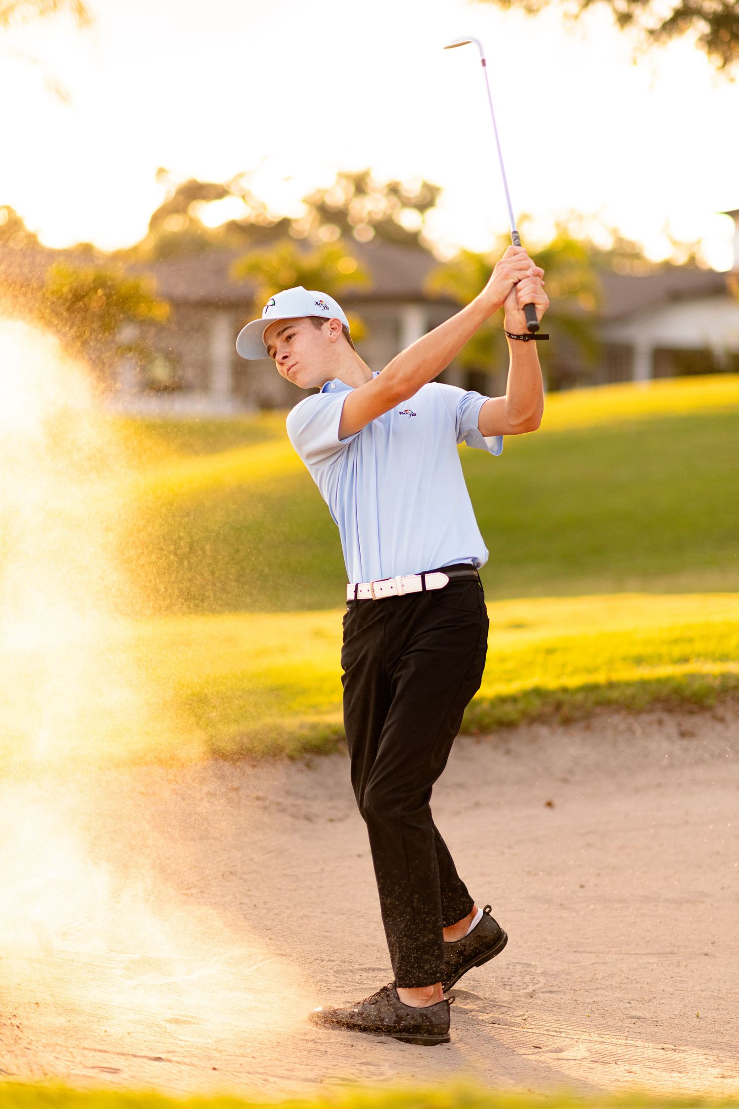 Young golfer swinging a club from a sand bunker on a golf course at golden hour.