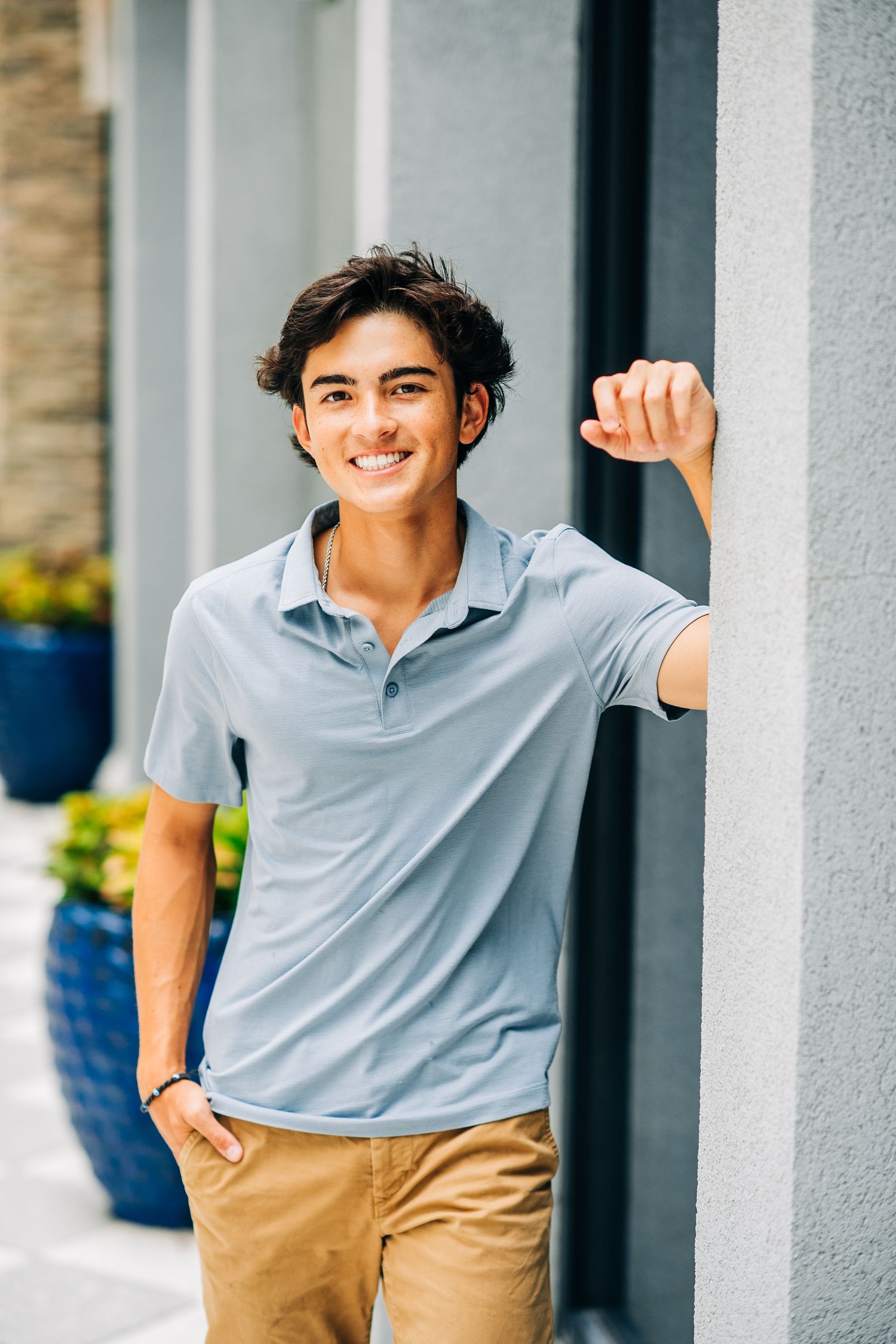 Smiling teen in blue polo leaning against wall outdoors.