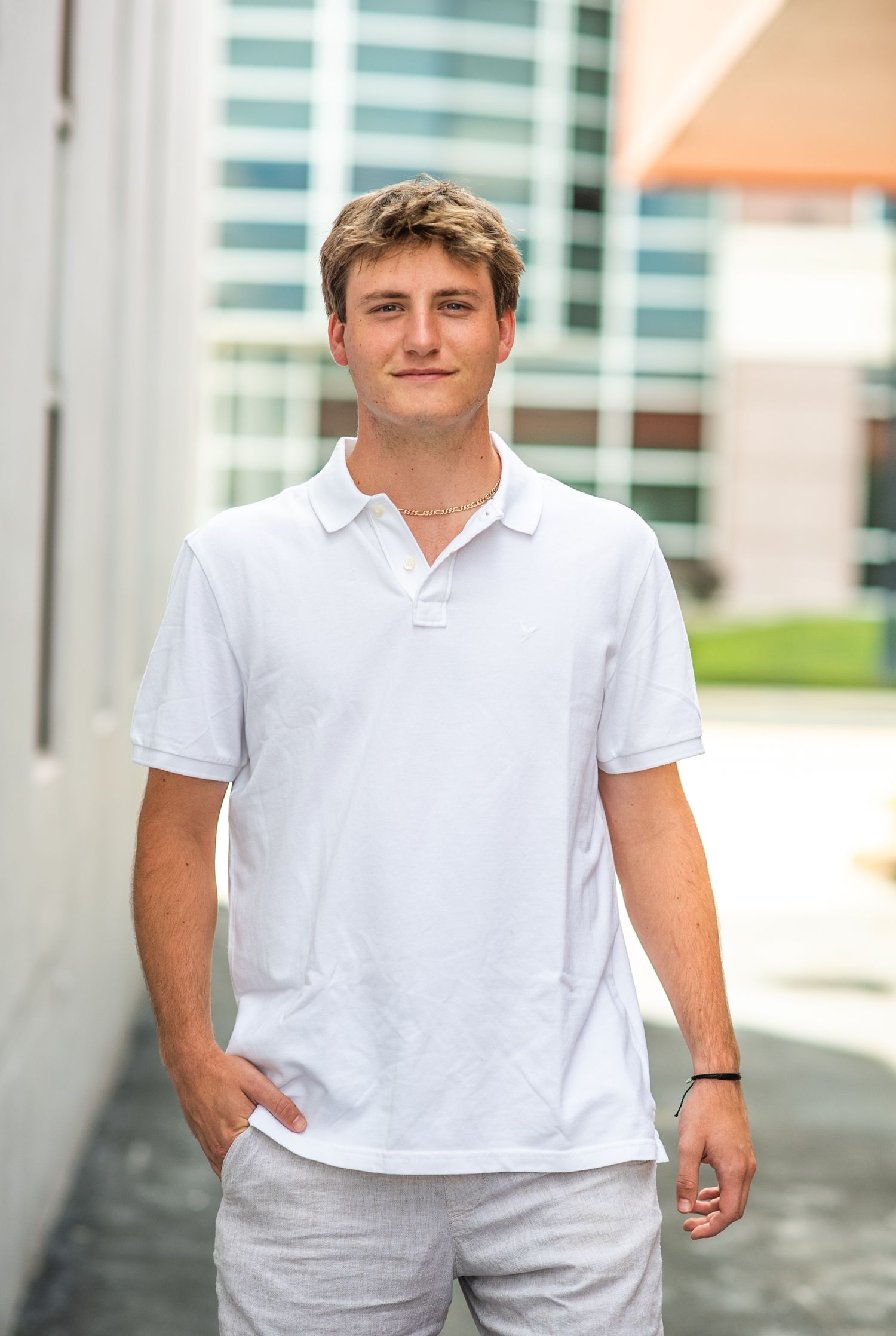Young man in white polo shirt smiling outdoors near modern building.