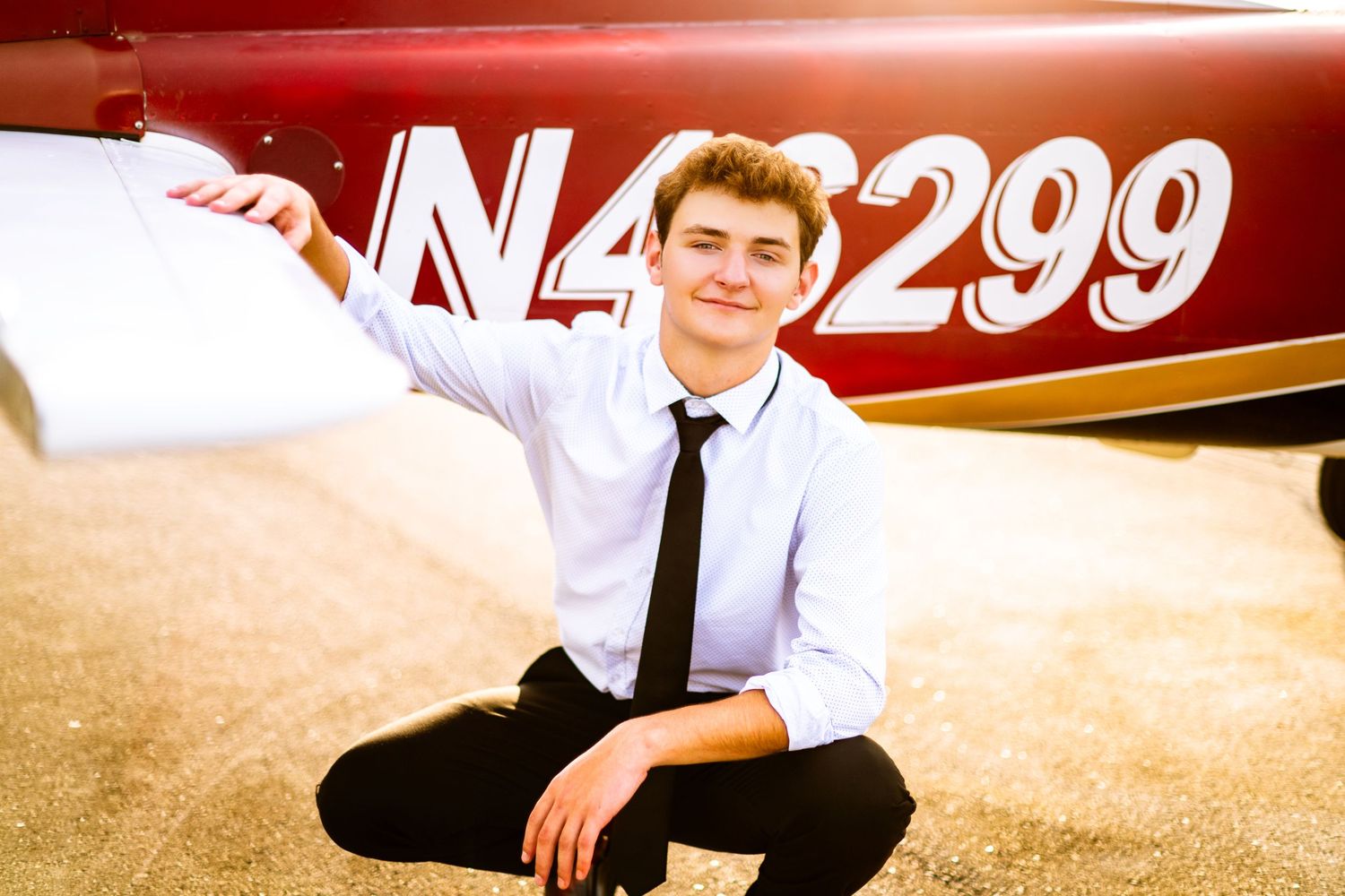 Young man in white shirt and tie crouching beside a red aircraft with registration number N45299.