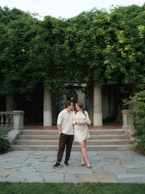 Couple poses together on stone patio before ivy-covered classical columns at elegant outdoor venue.