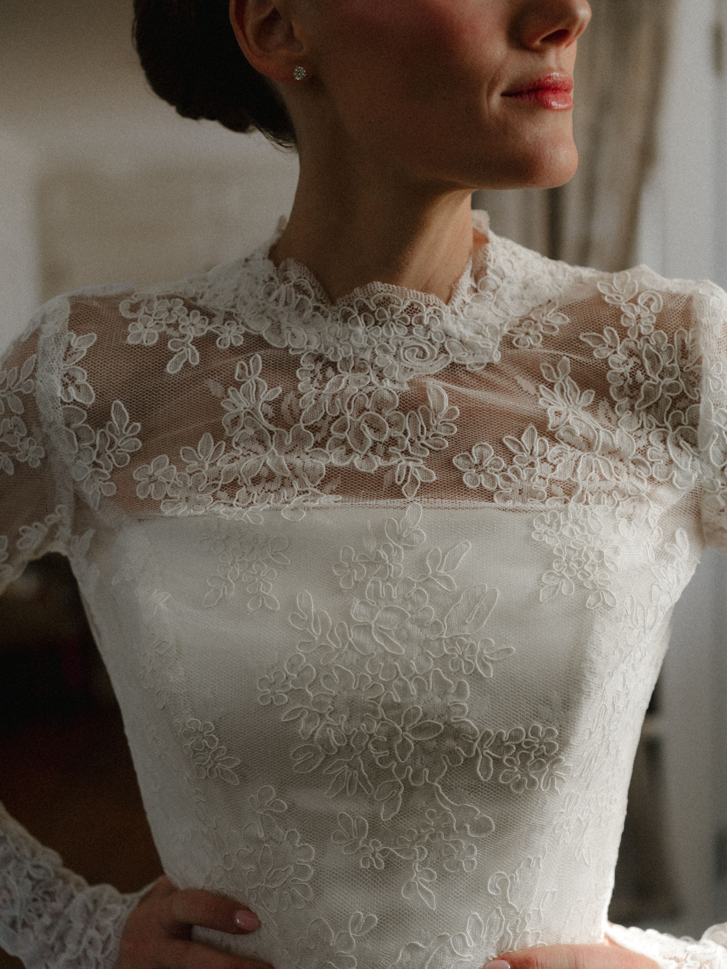 Close-up of a bride wearing an elegant ivory lace wedding gown with floral embroidery and sheer neckline.