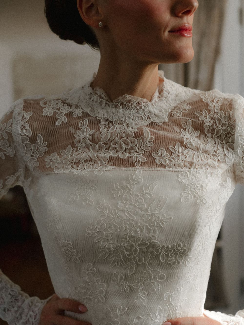 Close-up of a bride wearing an elegant ivory lace wedding gown with floral embroidery and sheer neckline.