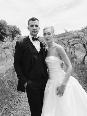 Elegant bride and groom posing in a vineyard, wearing a white ball gown and black tuxedo in a black and white photo.
