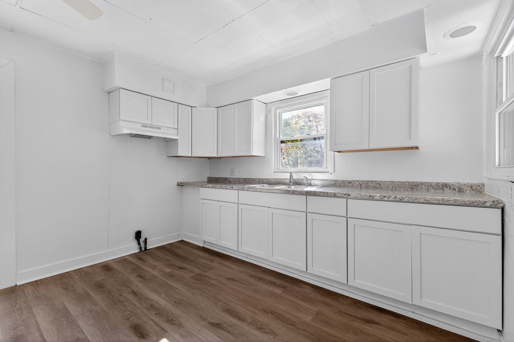Modern kitchen with white shaker cabinets, granite countertops, dark hardwood floors, and a window above the sink.
