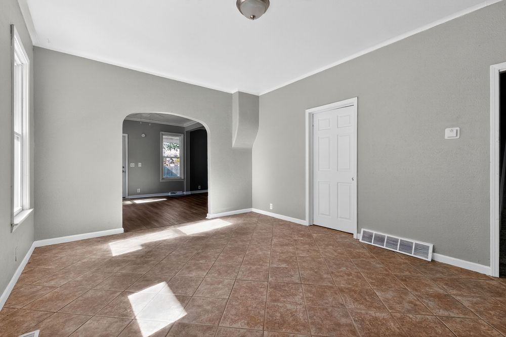 Spacious living room with gray walls, tile floors, crown molding, and an arched doorway leading to a second room.
