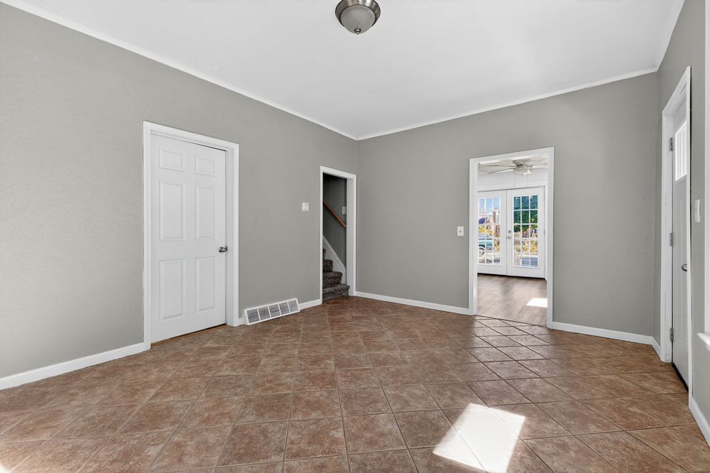 Spacious empty room with gray walls, crown molding, tile flooring, and a white door leading to a staircase.