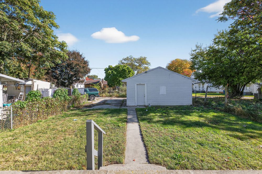 A detached white garage with a concrete path leading through a well-maintained green lawn surrounded by mature trees.