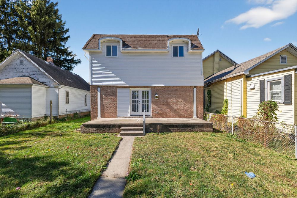 Two-story brick and siding home with dormers, covered porch, and well-maintained lawn in a residential neighborhood.