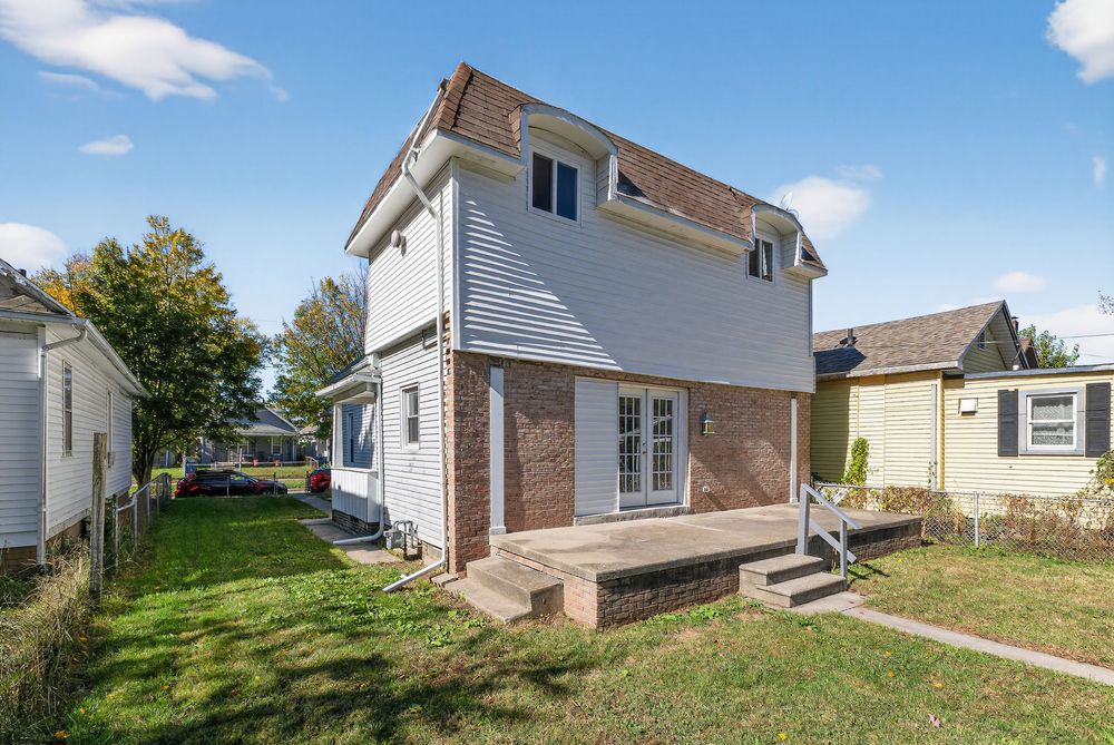 Two-story brick and vinyl siding home with covered porch, green lawn, and neighboring houses on a sunny day.