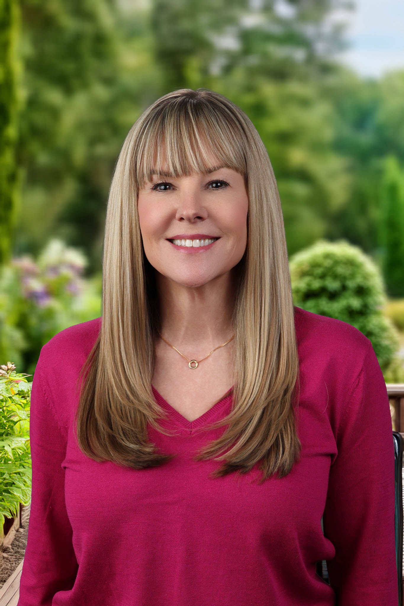 Professional Headshot Session with a realtor who has blonde hair wearing a pink top posing in a lush garden setting.
