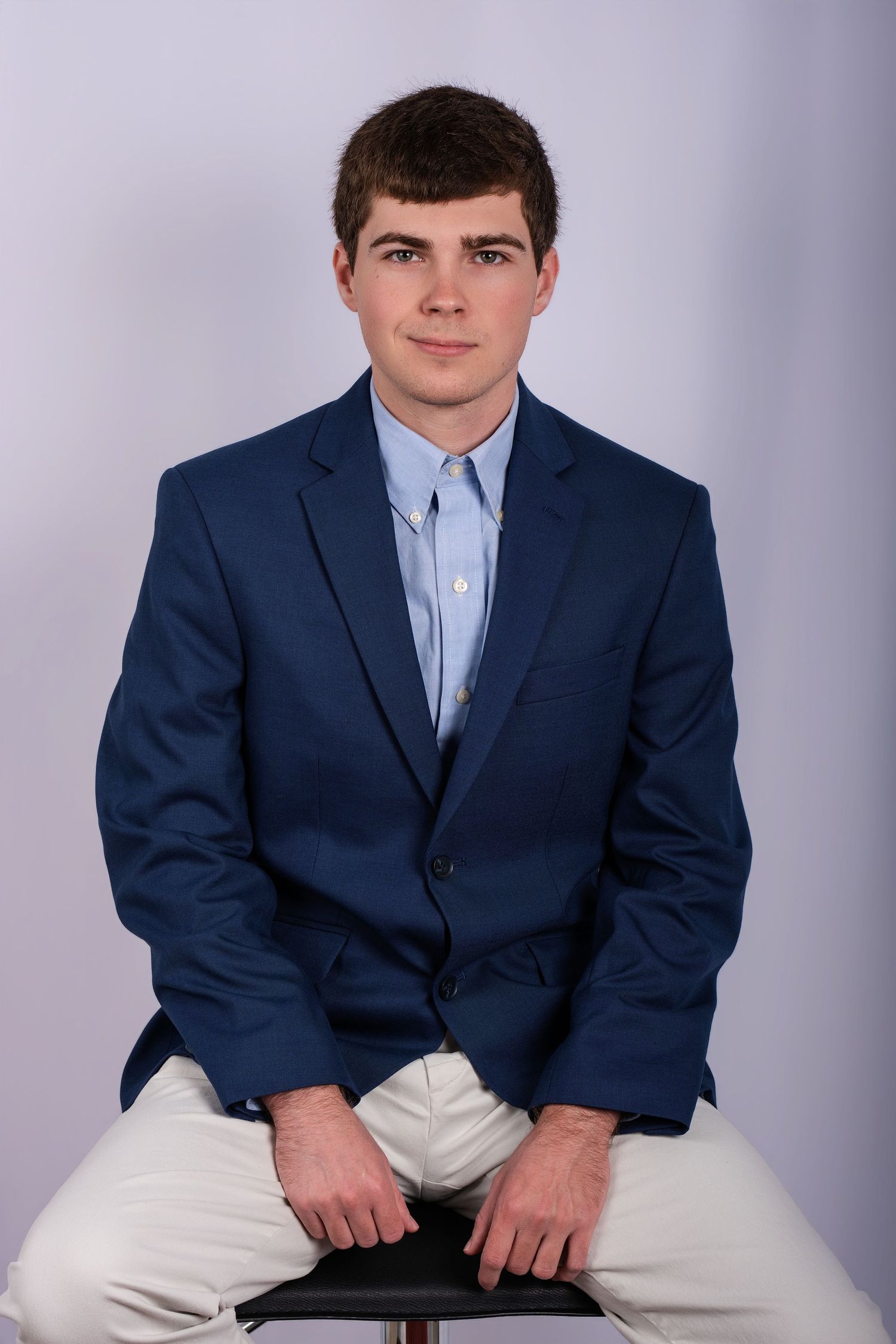 Professional Headshot Session with a young man in a navy blue blazer and light blue shirt seated on a stool.