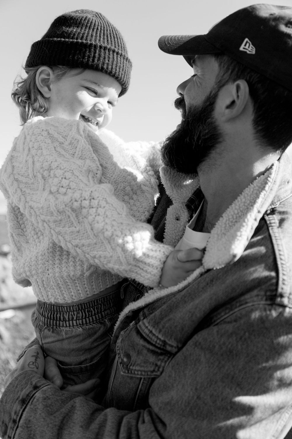 Close-up black and white photo of bearded dad and laughing toddler in knit sweater sharing a joyful moment.