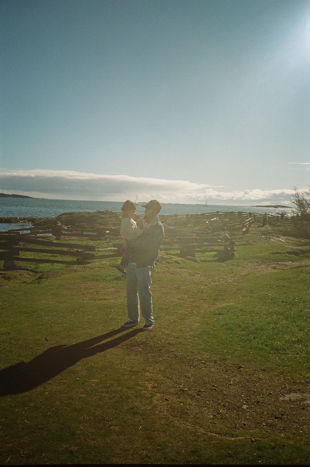 Silhouette of adult holding child against sunny coastal landscape with blue sky.
