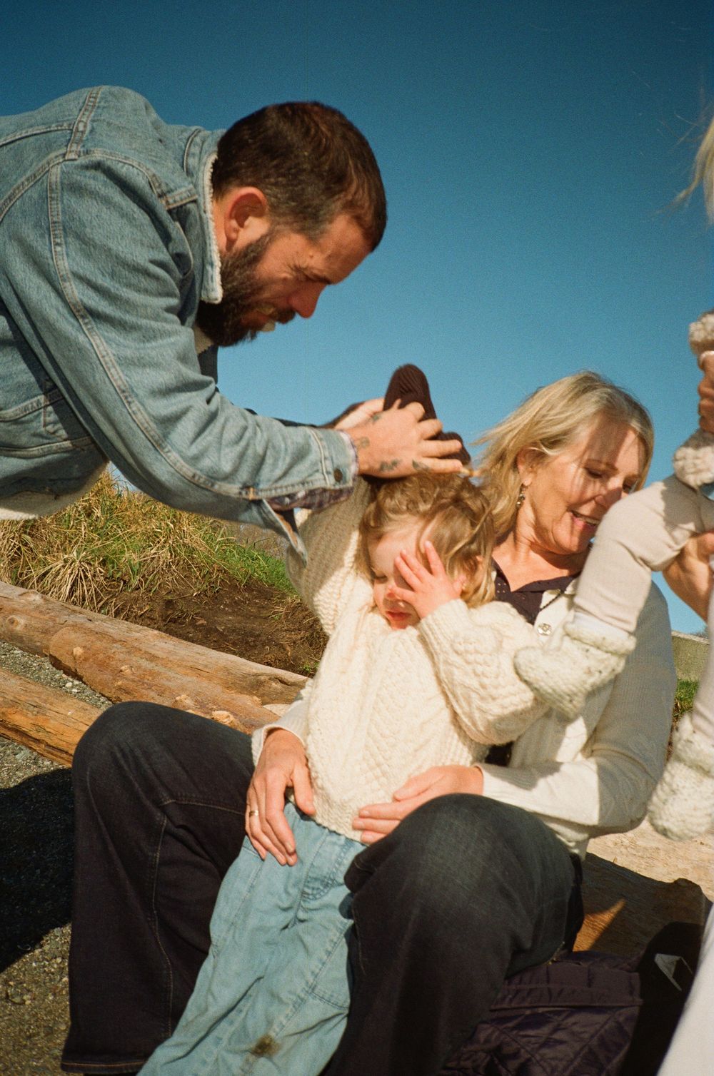 Bearded man and older woman tenderly comforting a young child outdoors on a sunny day.