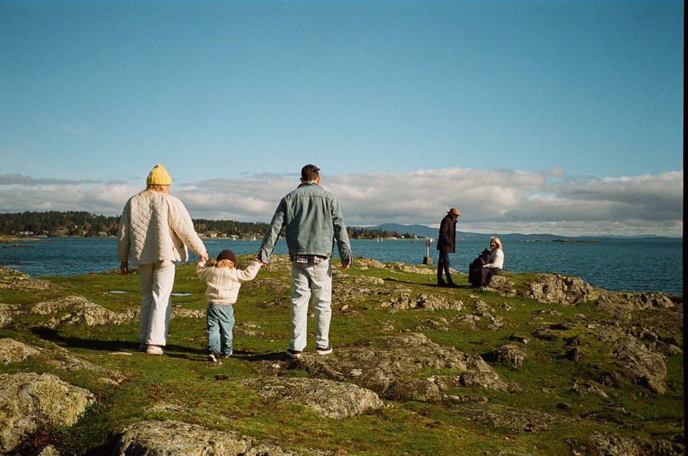 Family walking hand in hand across rocky coastal landscape under blue sky.